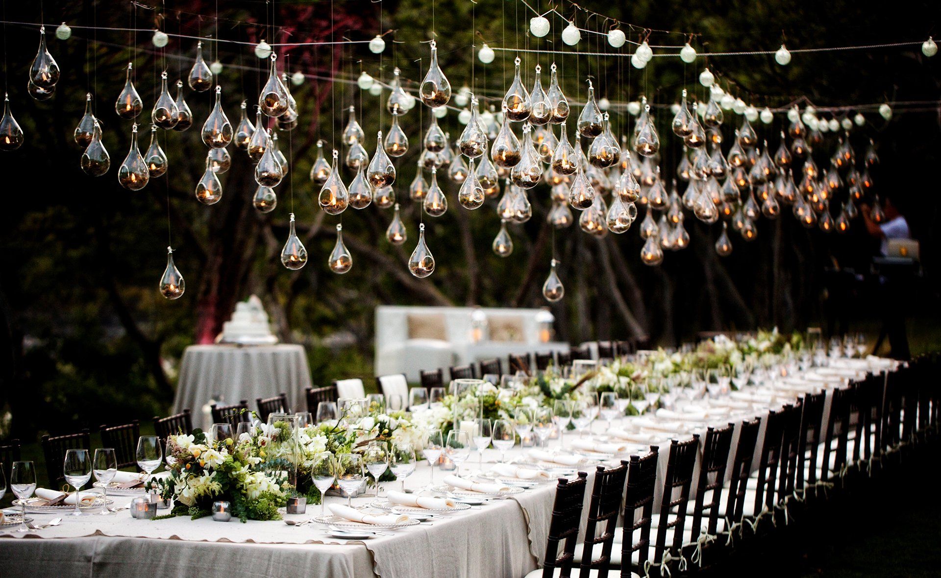 A long table with flowers and lights hanging from the ceiling.