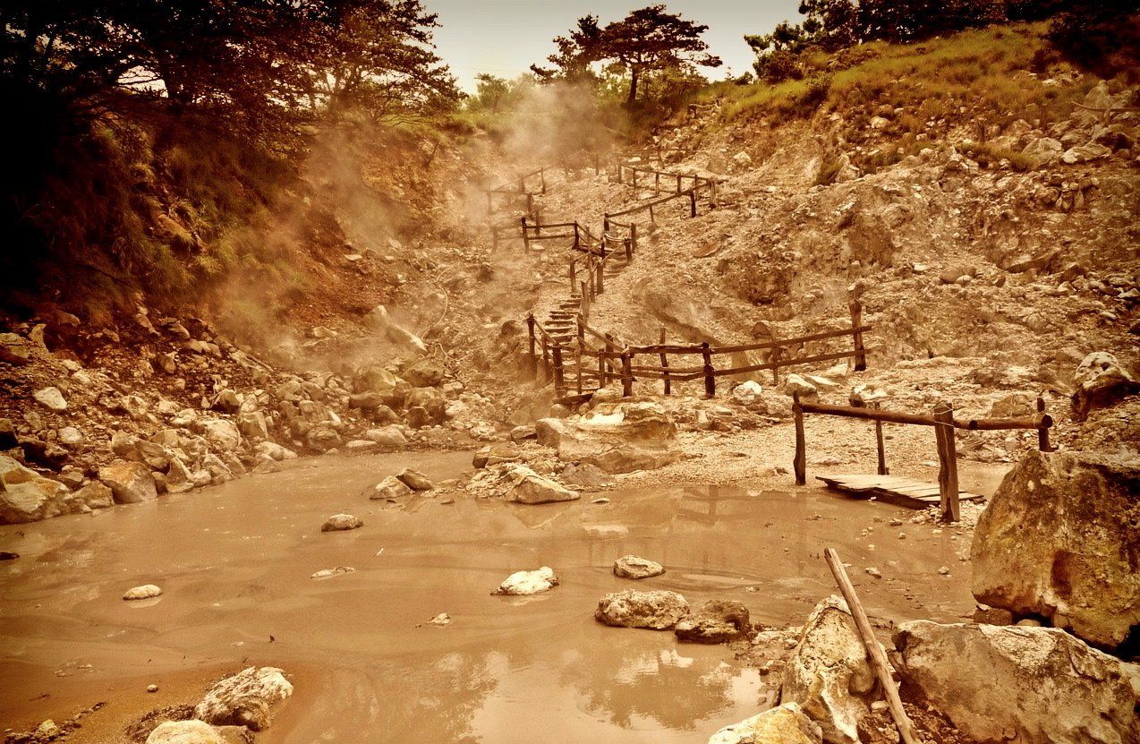 A muddy river surrounded by rocks and trees with a wooden fence.