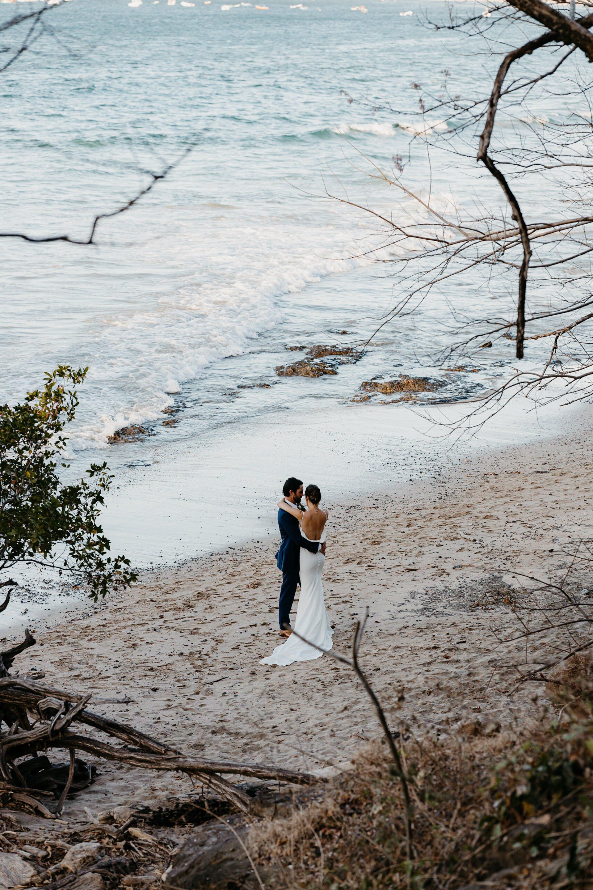A bride and groom are standing on a beach near the ocean.