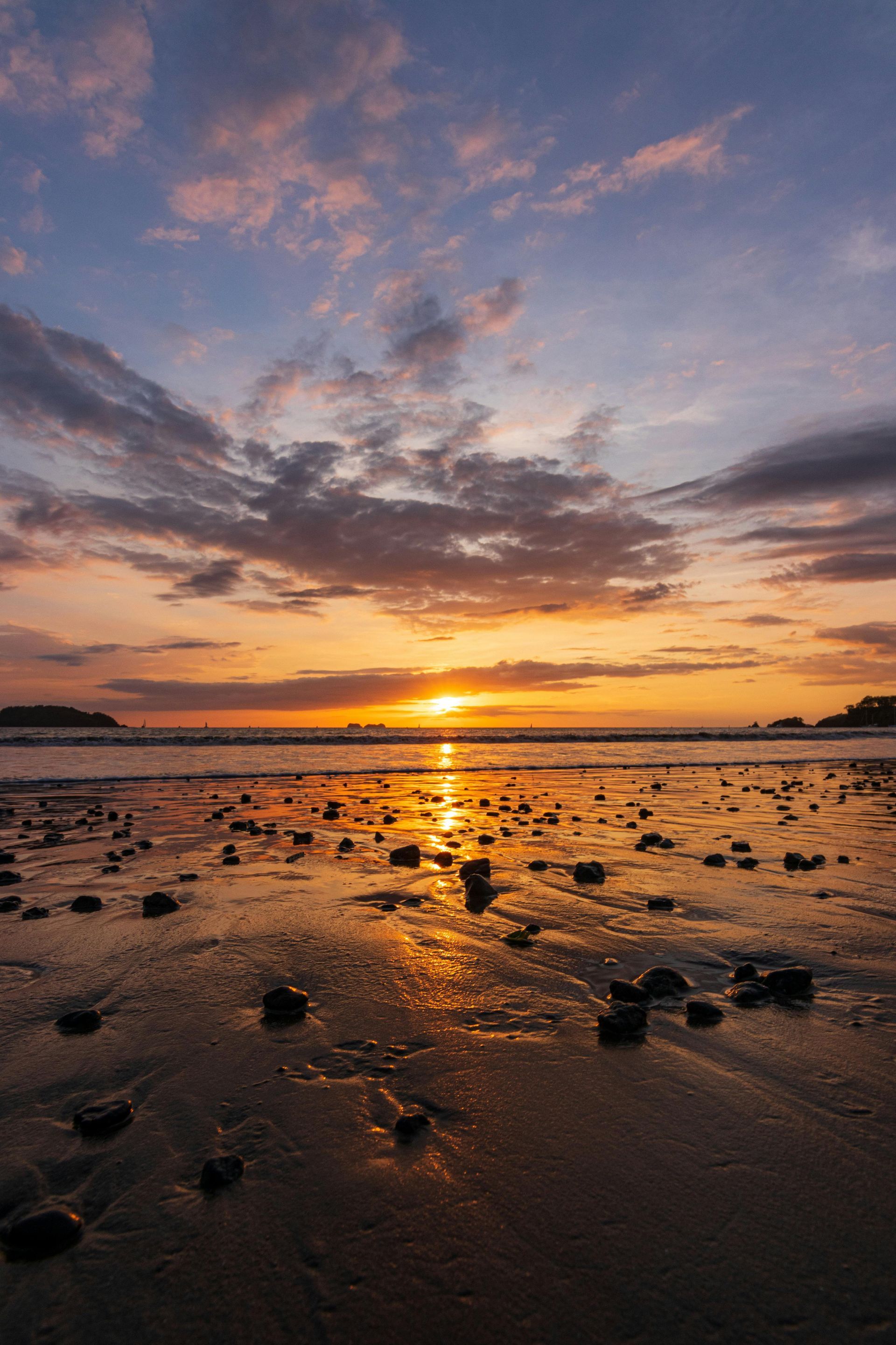 The sun is setting over the ocean on a rocky beach.