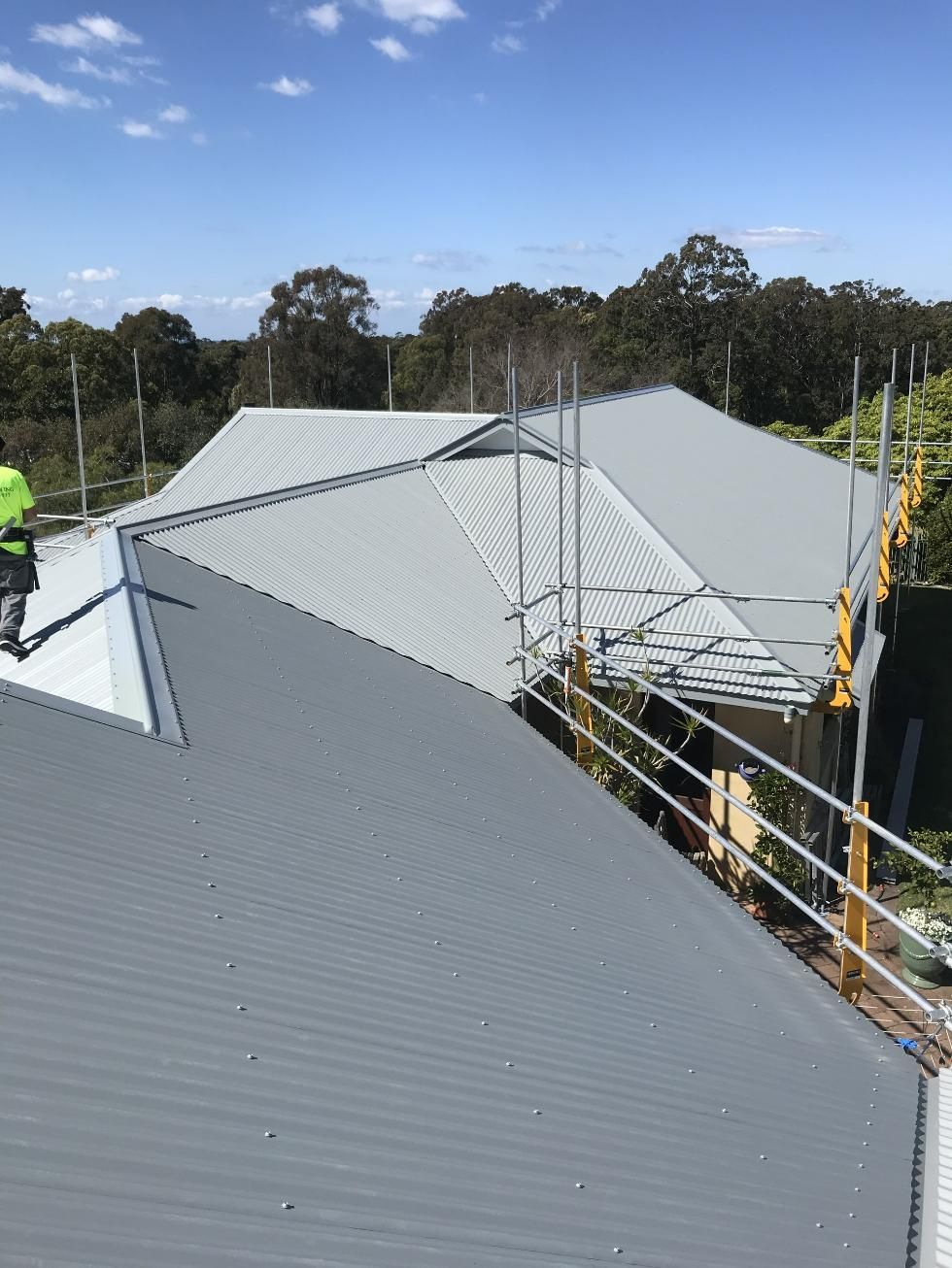 A Man Is Standing On The Roof Of A Building — Glenroofing Pty Ltd In Taree, NSW