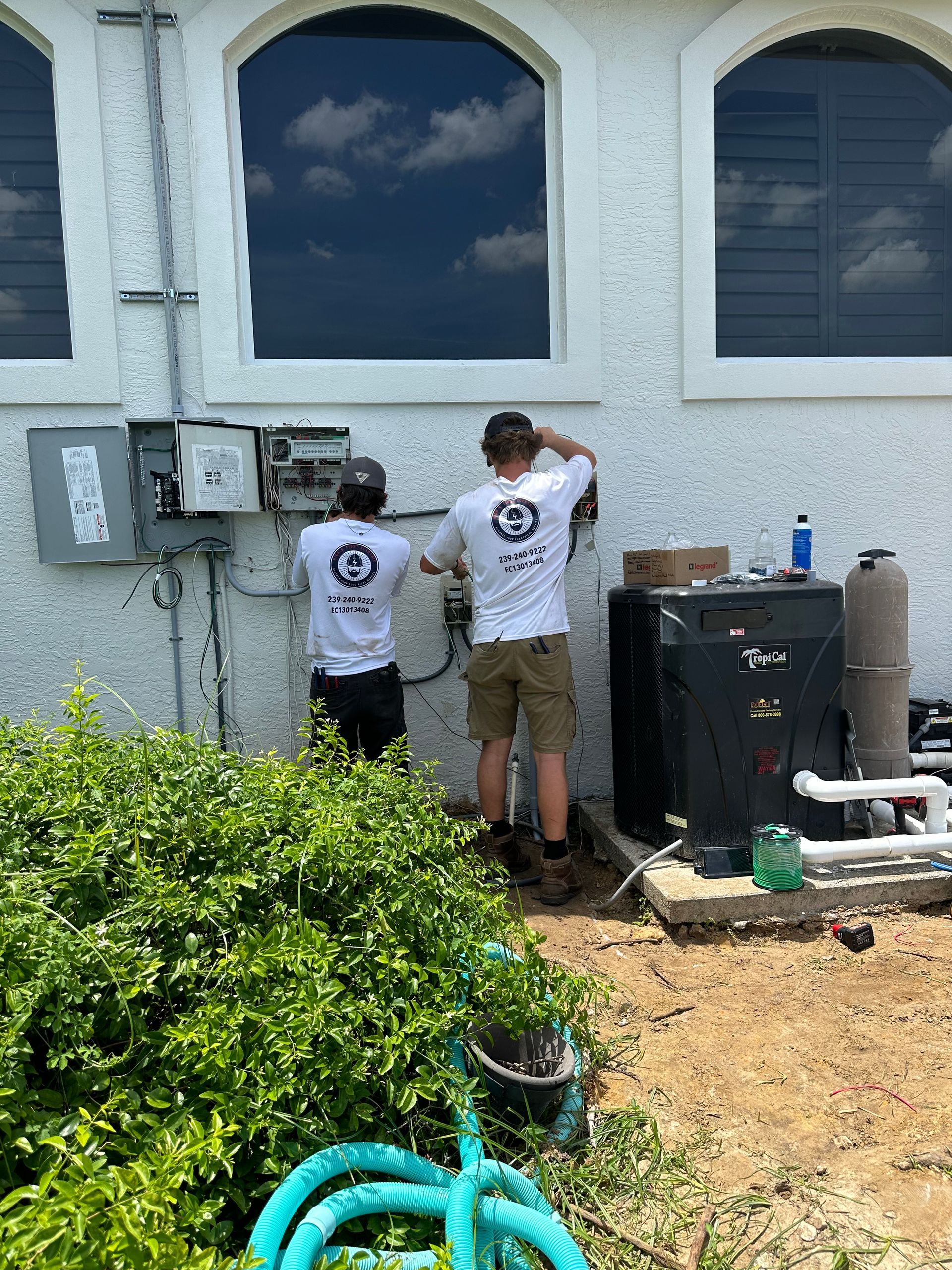 Two men are working on a pool pump outside of a house.