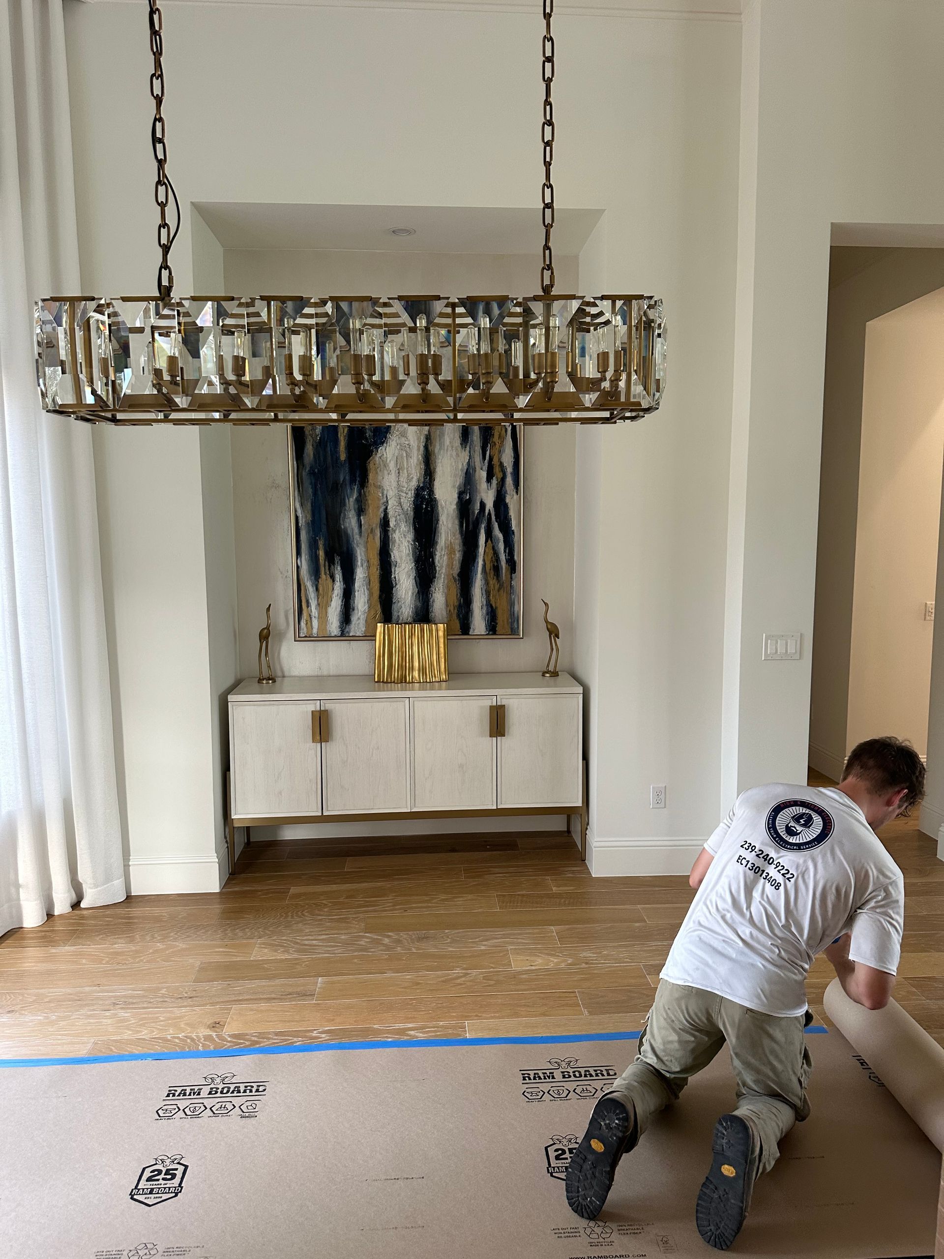A man is kneeling on the floor in a room with a chandelier hanging from the ceiling.