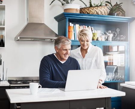 A man and a woman are looking at a laptop in a kitchen.