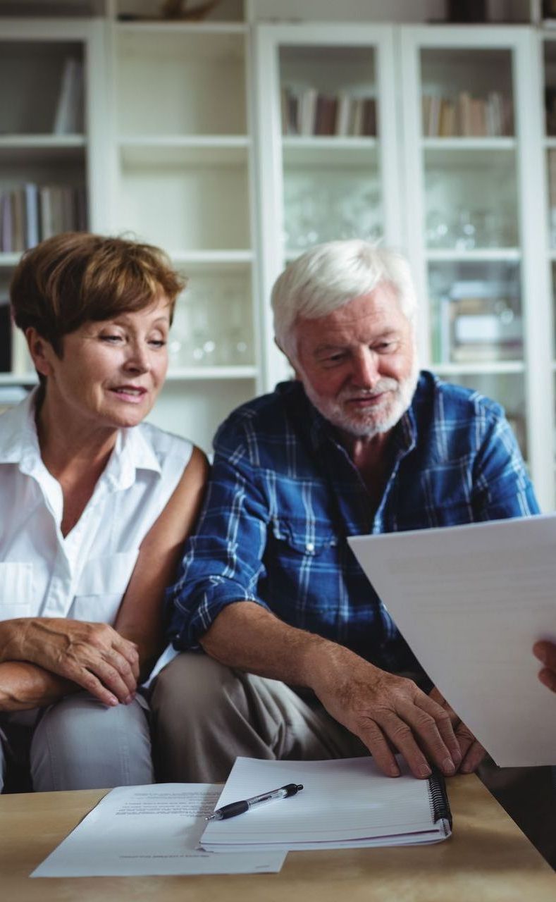 An elderly couple is sitting at a table looking at a piece of paper.