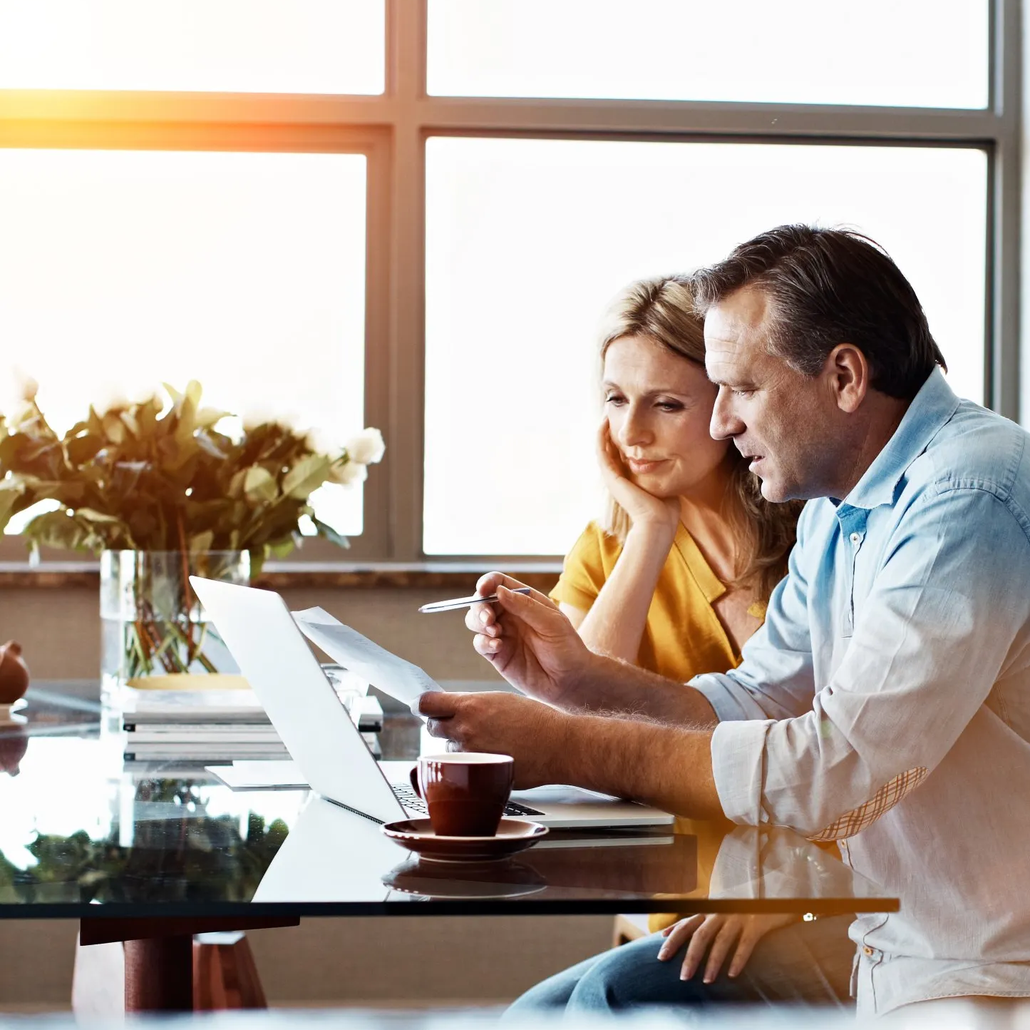 A man and a woman are sitting at a table looking at a laptop.