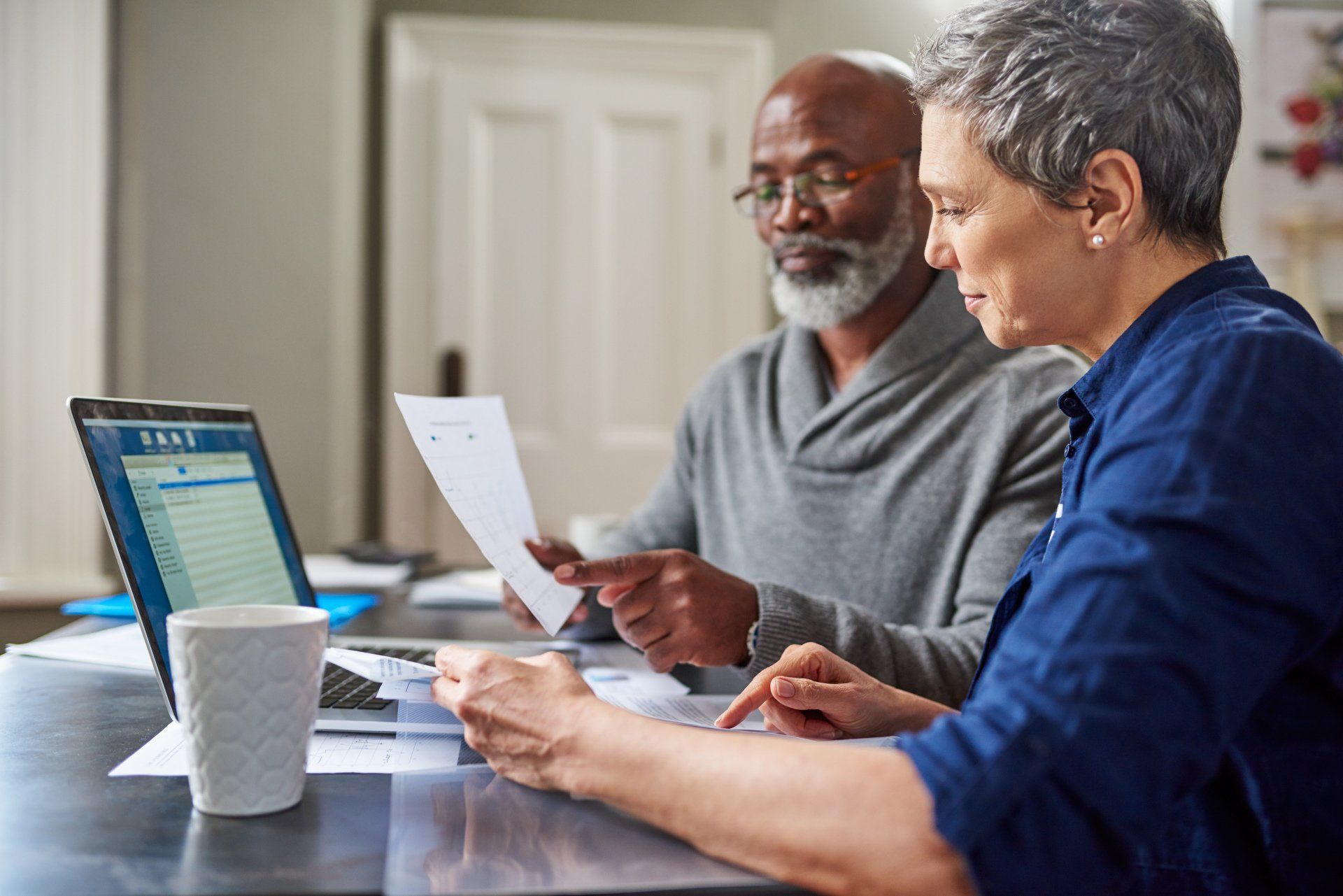 A man and a woman are sitting at a table with a laptop and papers.