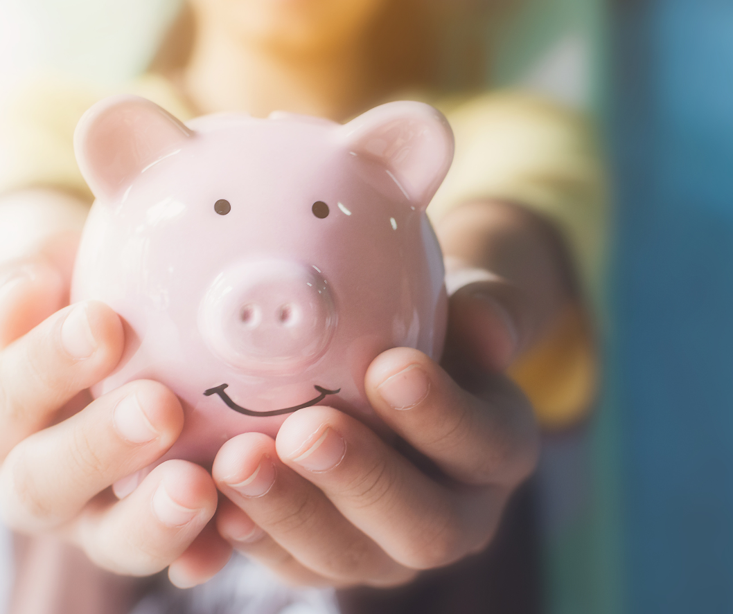 A person is holding a pink piggy bank with a smiling face on it.