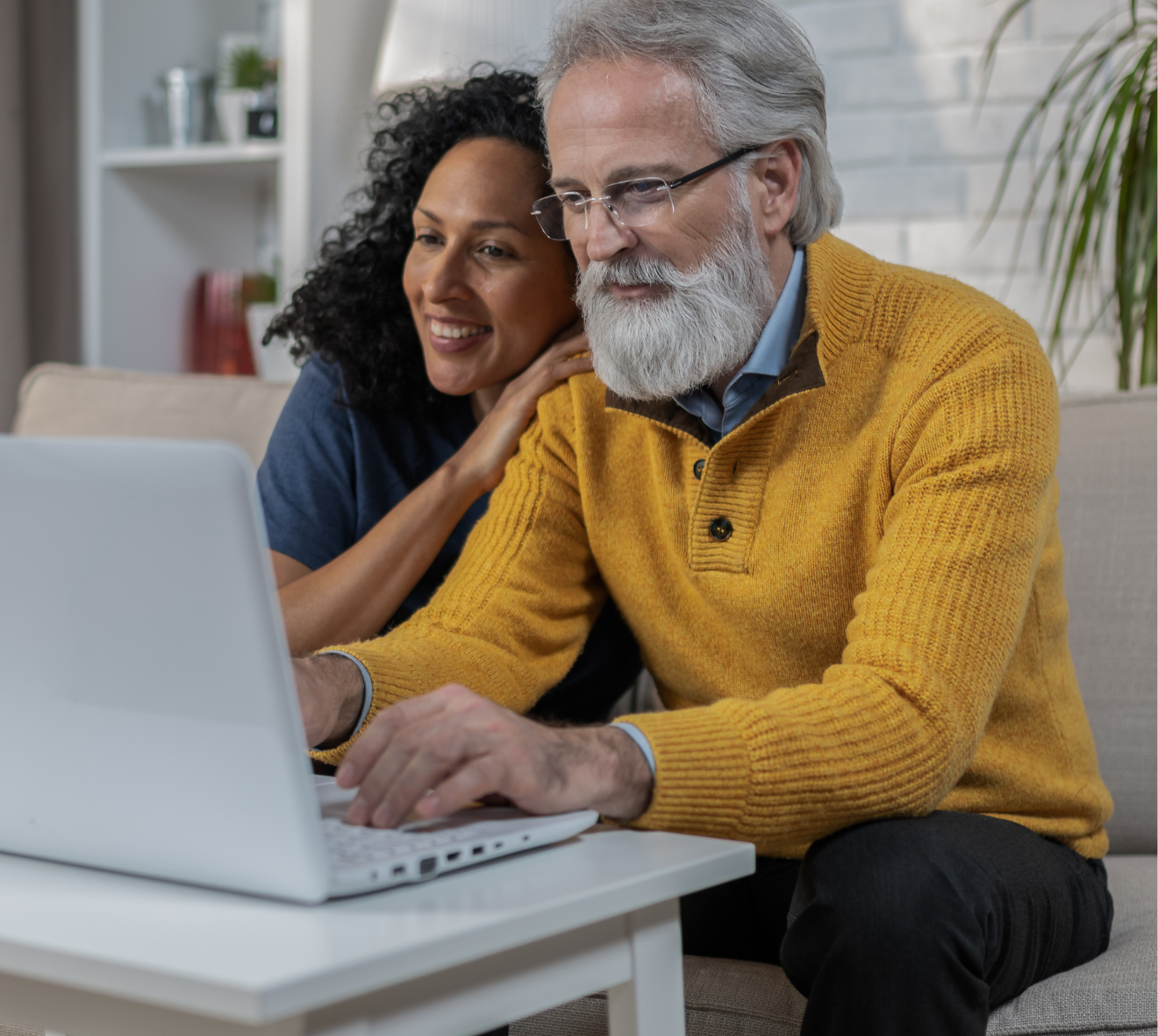 A man and woman are sitting on a couch looking at a laptop computer.