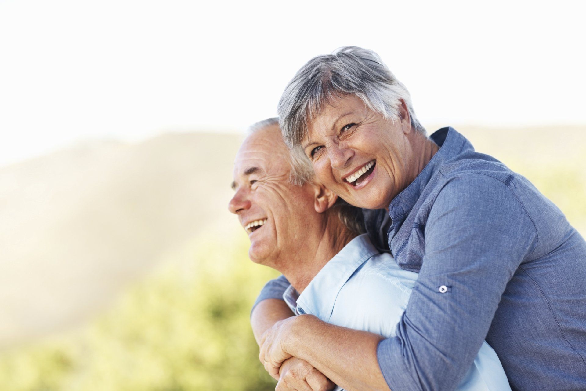 An elderly couple is hugging each other and smiling.