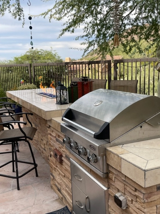 A stainless steel grill is sitting next to a table and chairs on a patio.