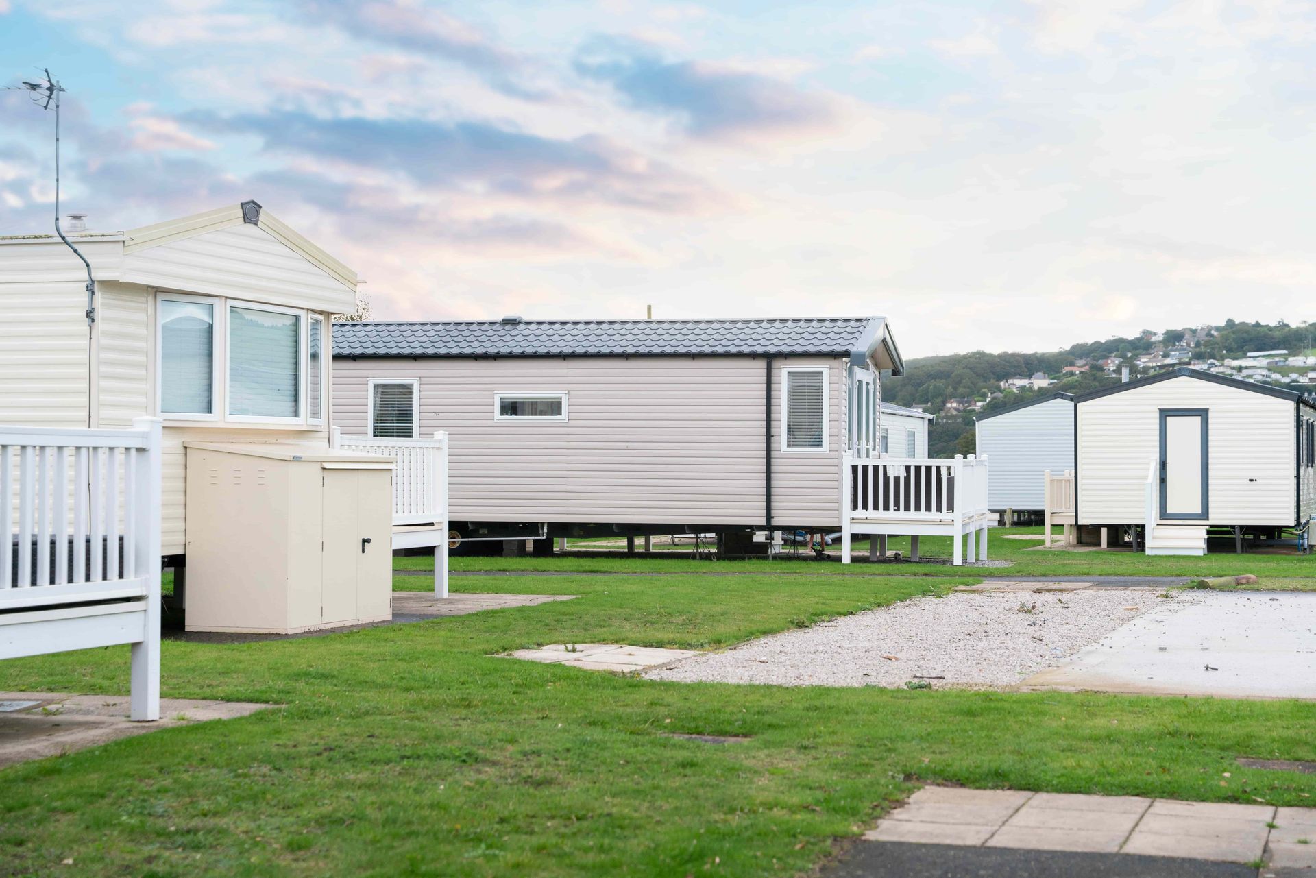 Several static mobile homes with white railings sit on a grassy plot under a soft, cloudy sky.