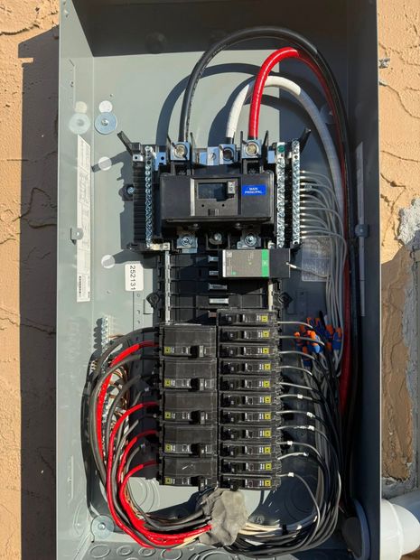 Electrical breaker panel with wiring and circuit breakers mounted on a gray board.