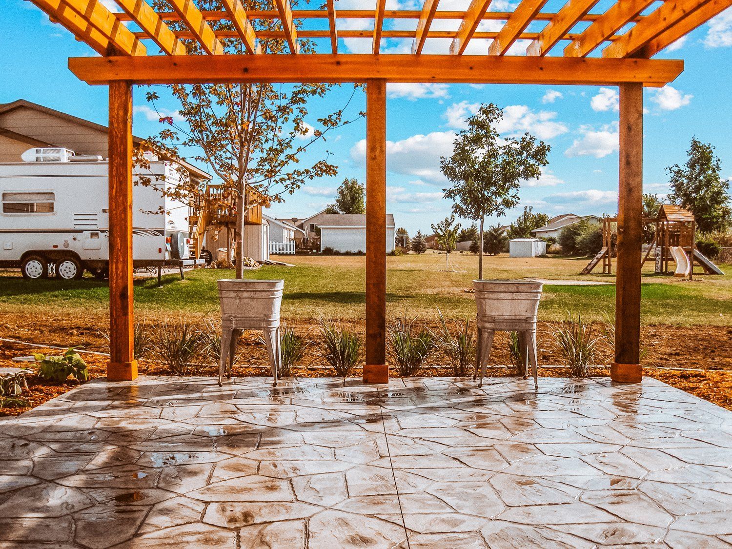 A wooden pergola over a patio with a rv parked in the background.