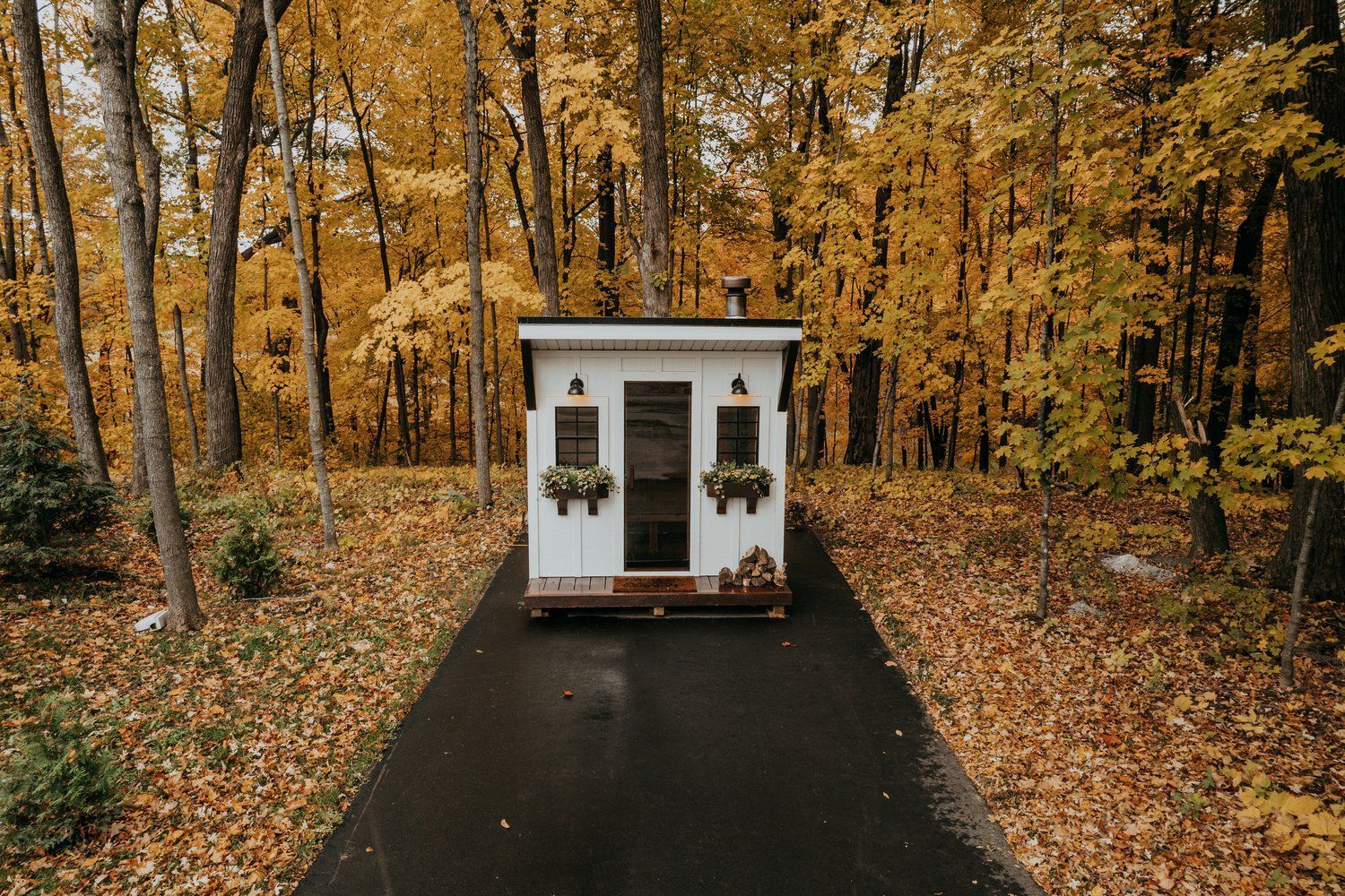 A small white house is sitting on the side of a road in the middle of a forest.