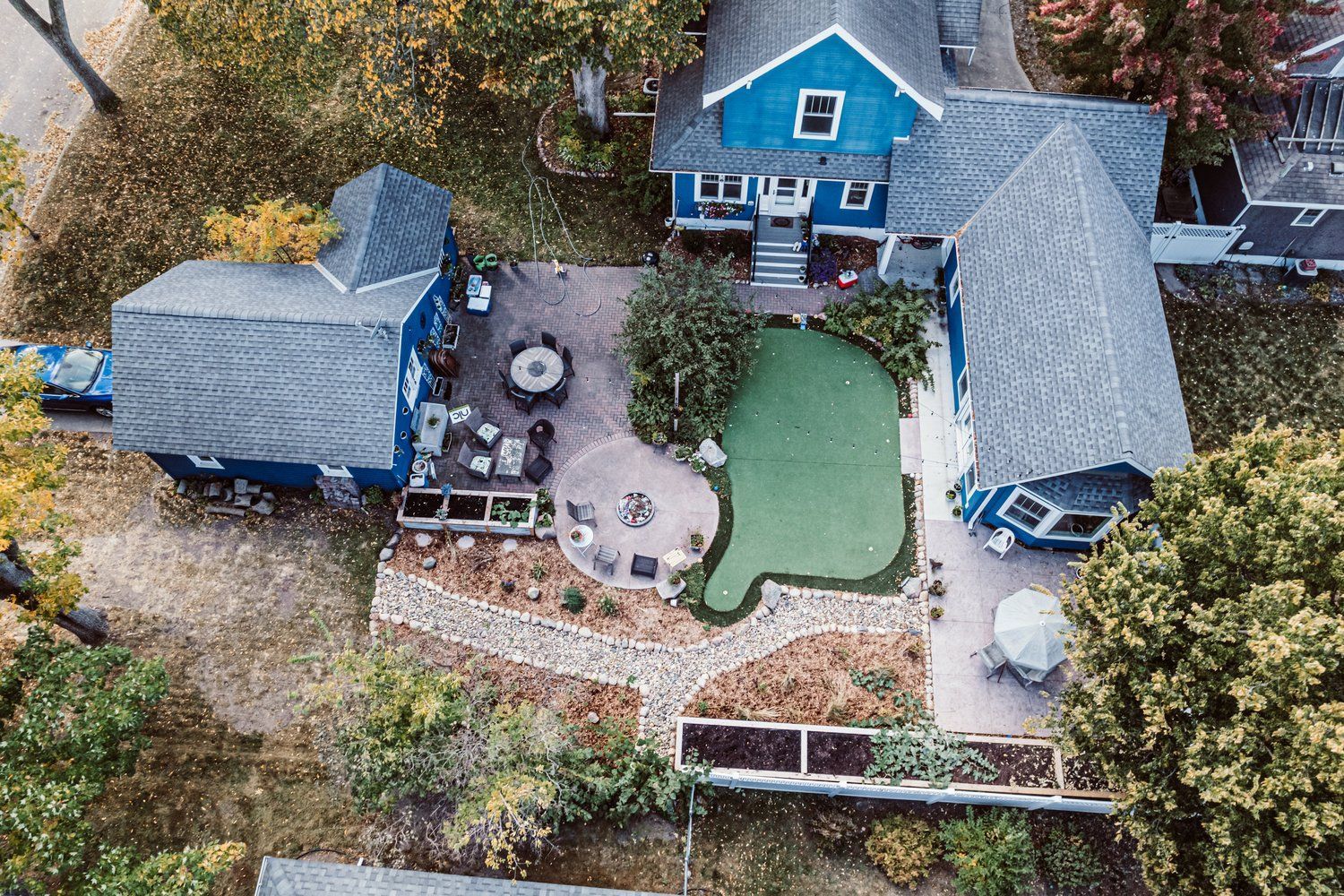 An aerial view of a large blue house with a green putting green in the backyard.