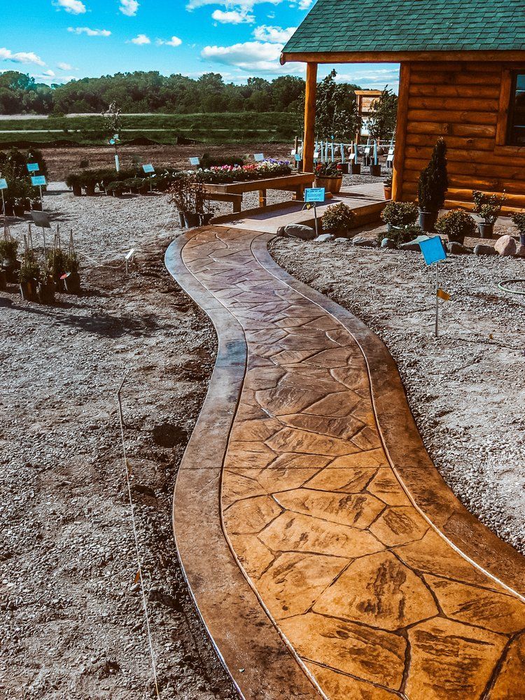 A concrete walkway leading to a log cabin in the middle of a dirt field.