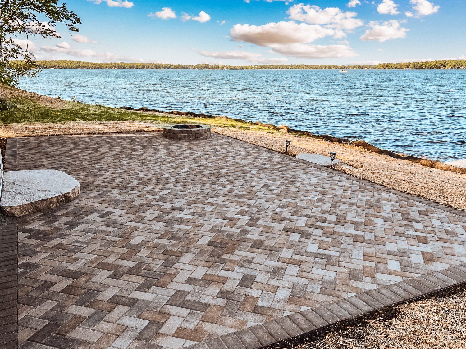 A patio with a fire pit and a view of a lake.