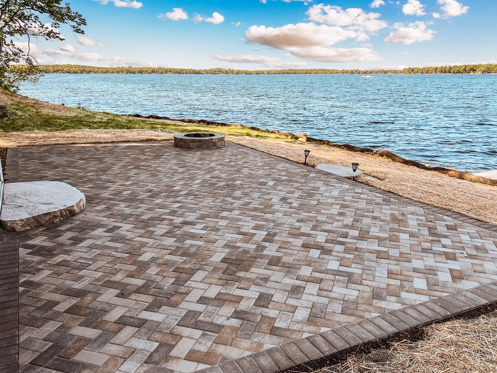 A patio with a fire pit and a view of a lake.