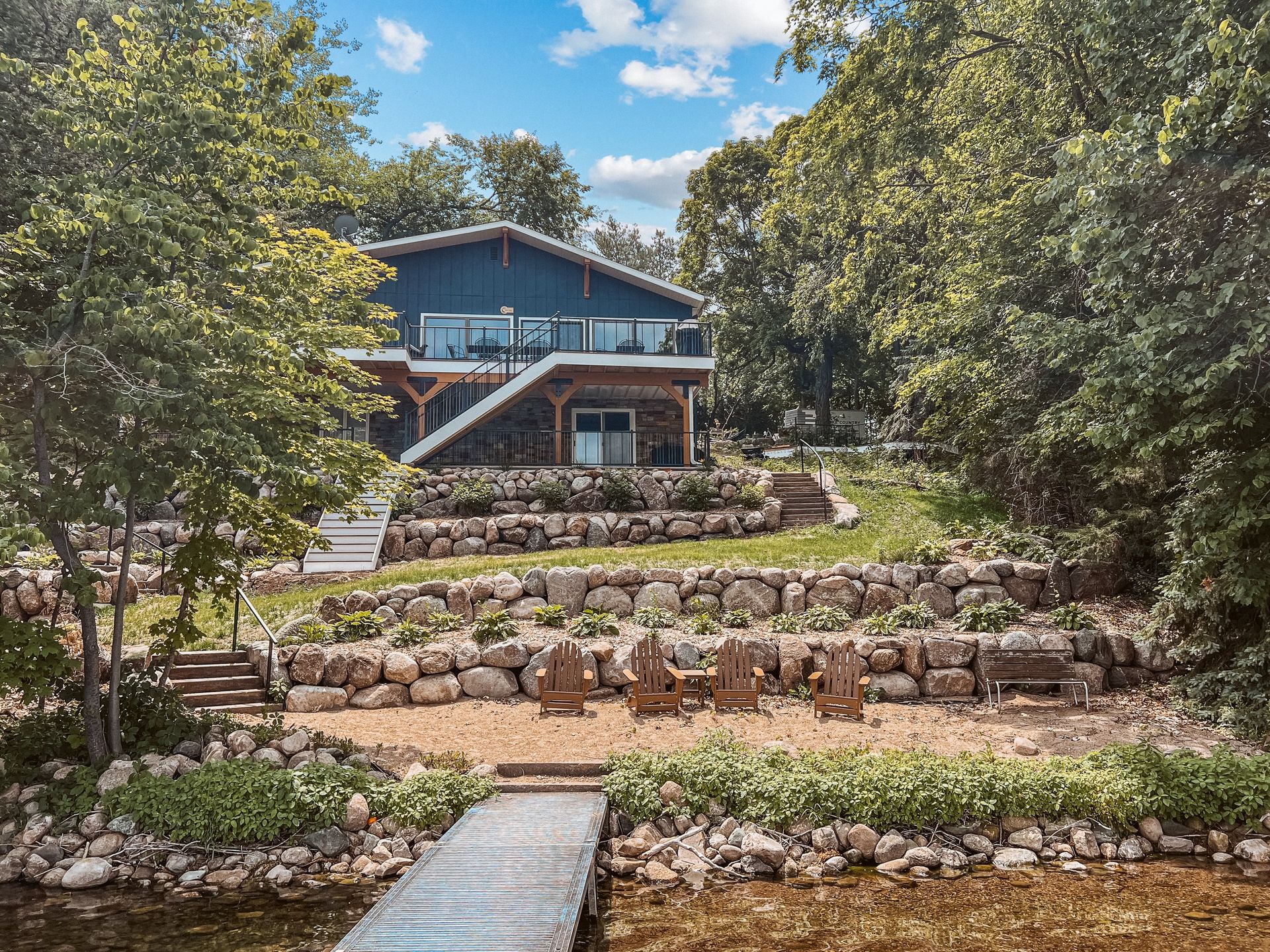 A large house with a dock in front of it is surrounded by trees and rocks.