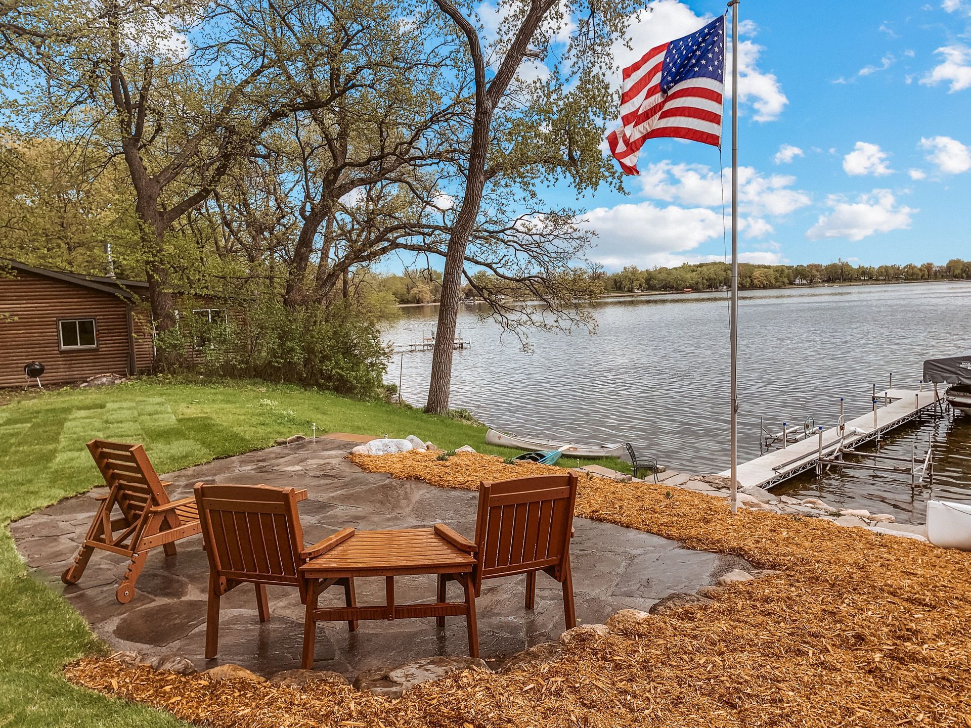 A patio with chairs and a table next to a lake with an american flag.