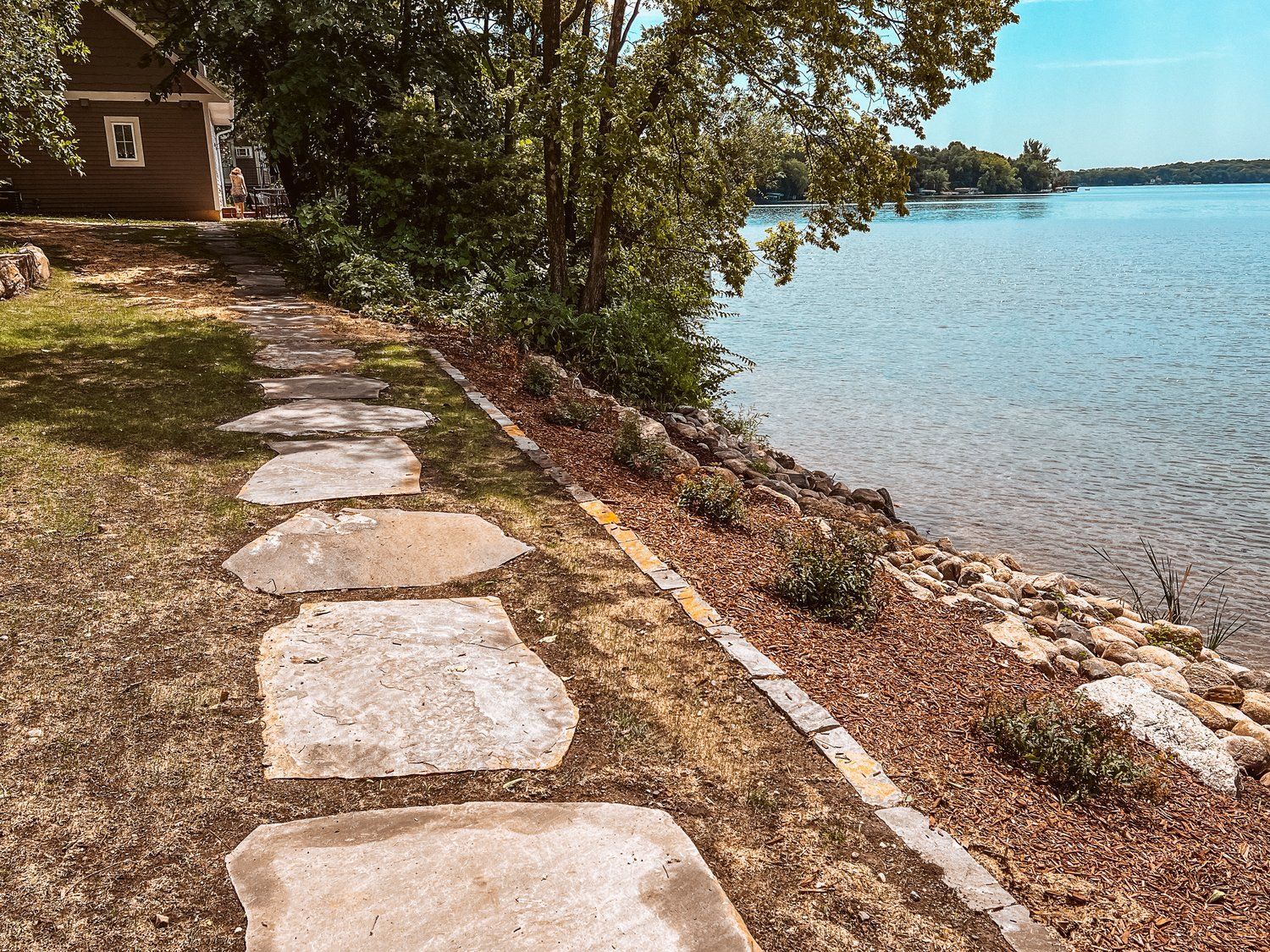 A stone walkway leading to a lake with a house in the background.