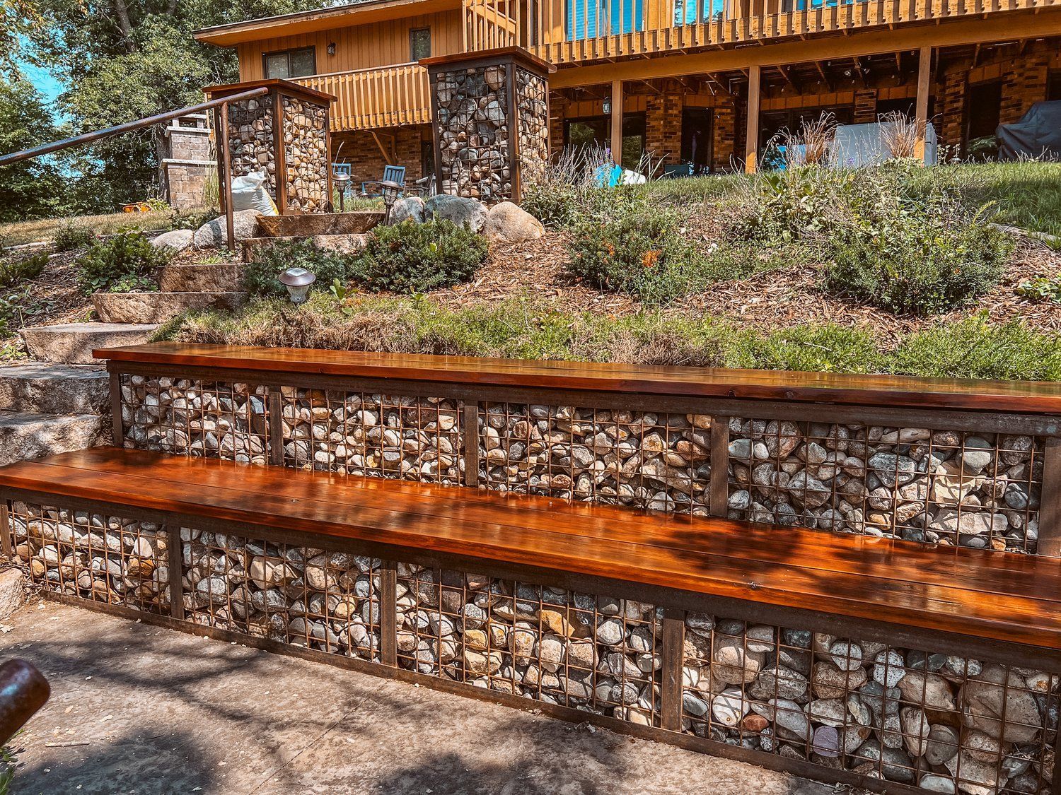 A wooden bench is sitting next to a stone wall in front of a house.