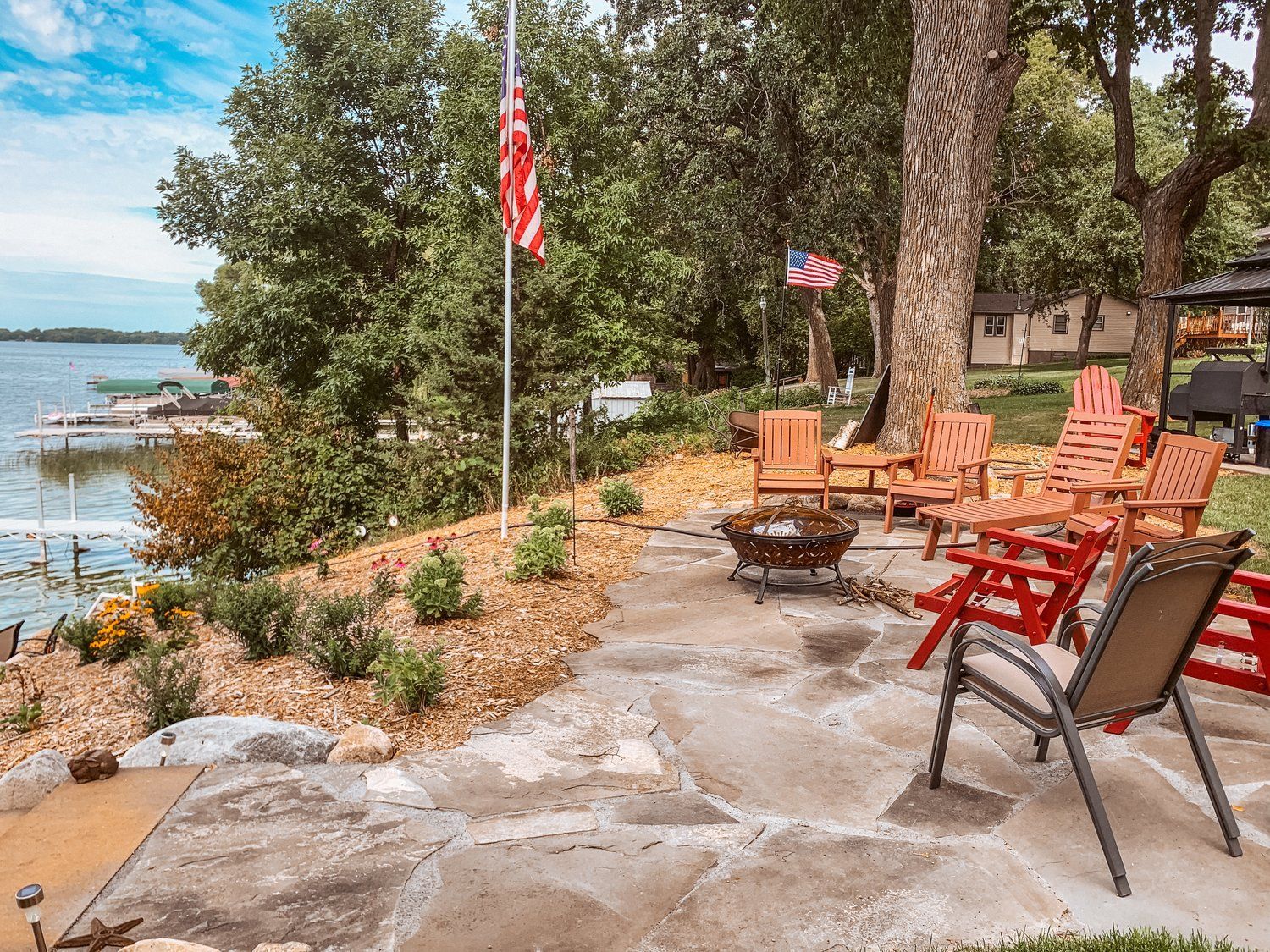 A patio with chairs and a fire pit next to a lake.