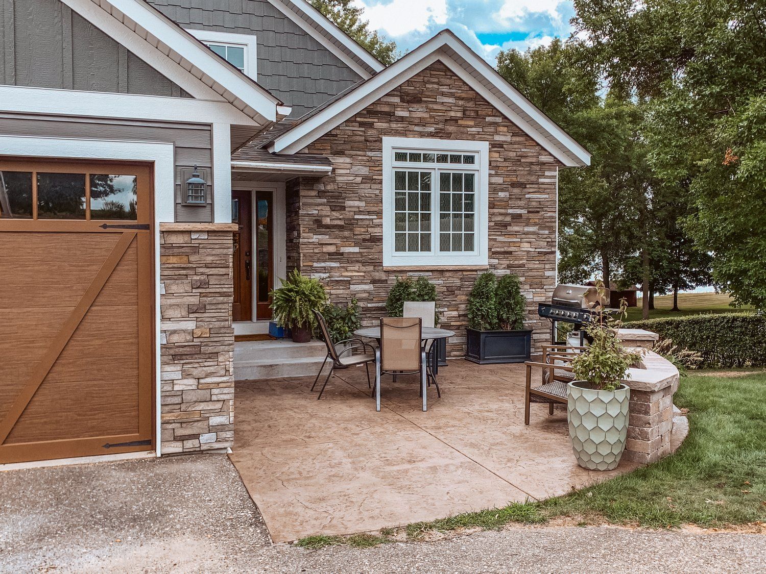 A stone house with a wooden garage door and a patio with a table and chairs.