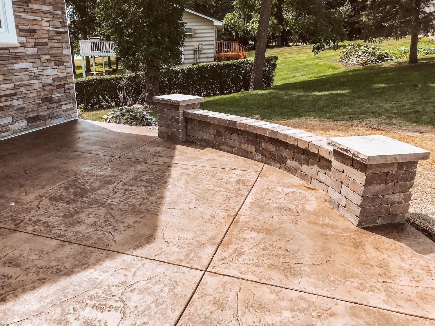 A concrete walkway with a stone wall and a bench in front of a house.