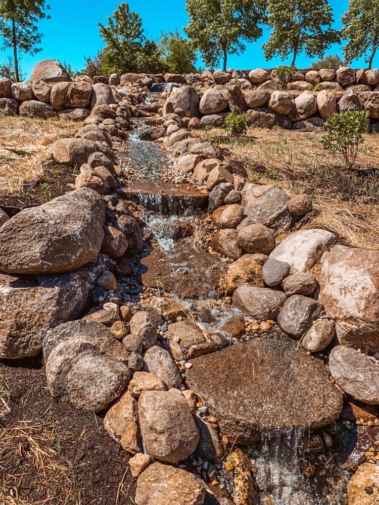 A small waterfall is surrounded by rocks in a park.