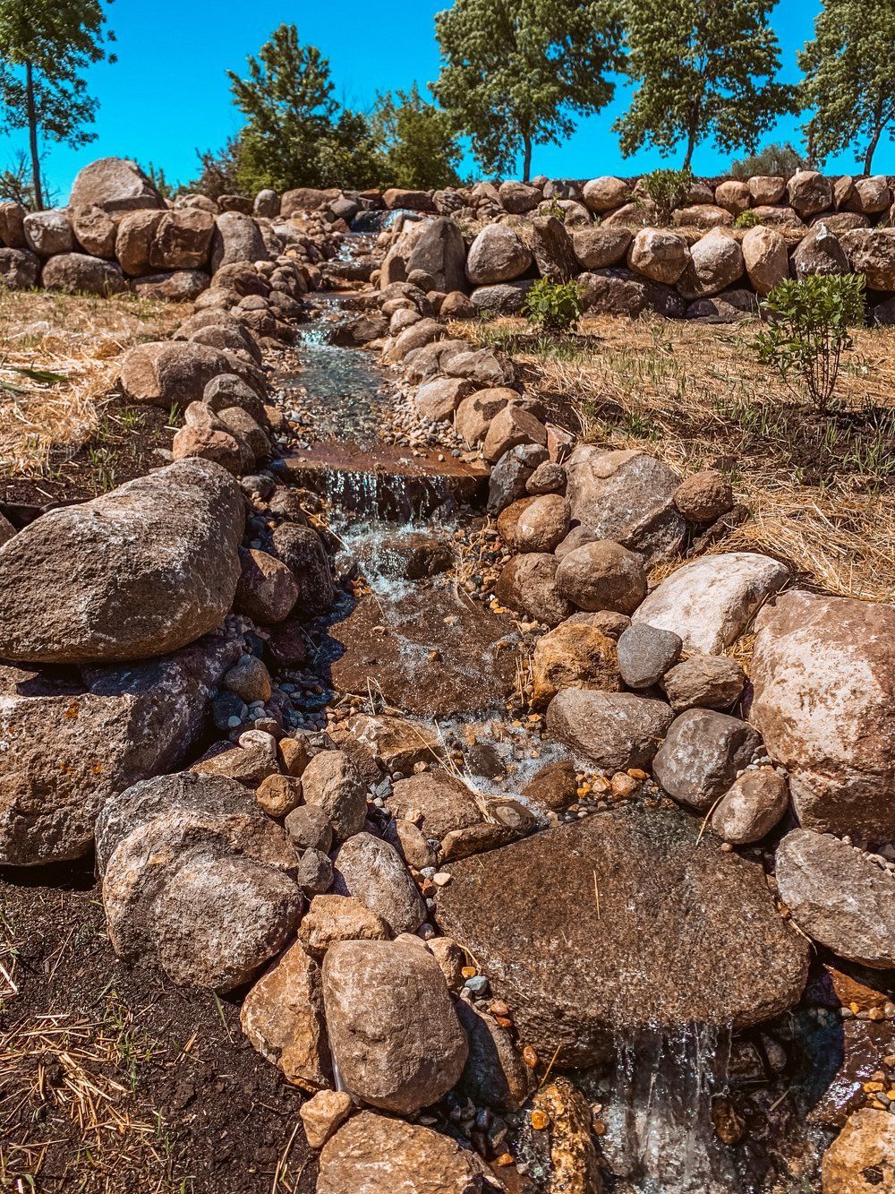 A stream of water flowing through a rocky area with trees in the background.