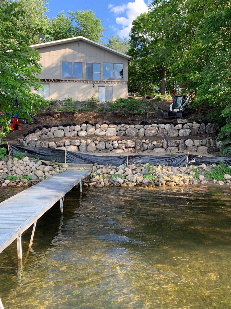 A house is sitting on top of a hill next to a lake with a dock in front of it.