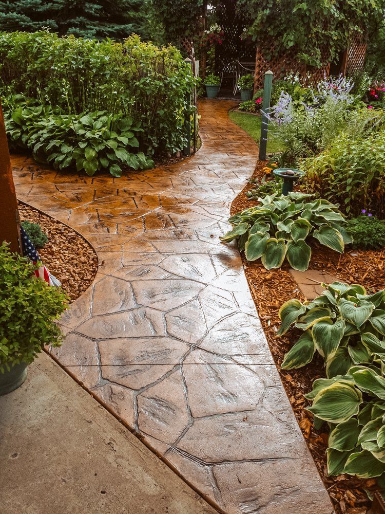 A concrete walkway in a garden surrounded by plants and bushes.