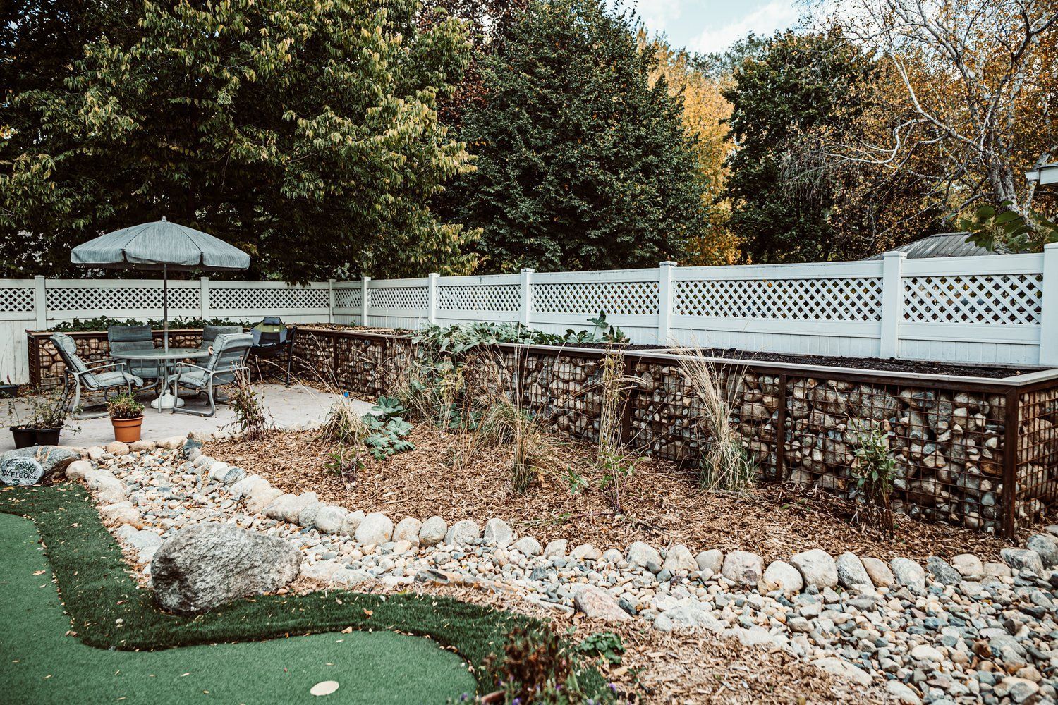 A backyard with a fence , a patio , and a small golf course.