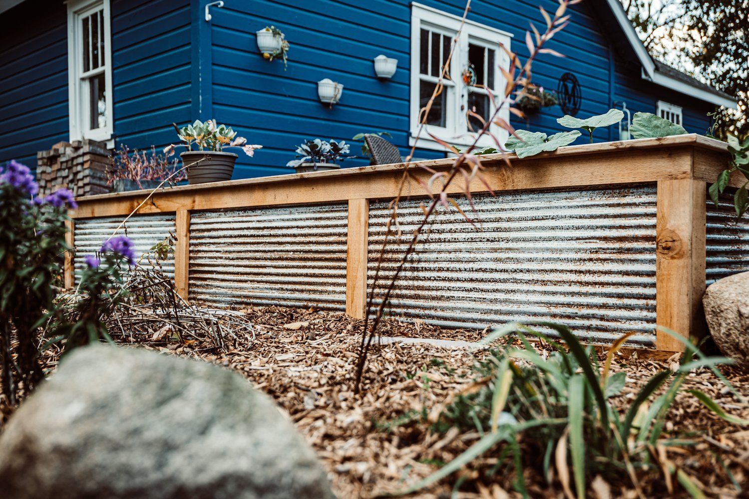 A blue house with a wooden deck and a metal fence in front of it.