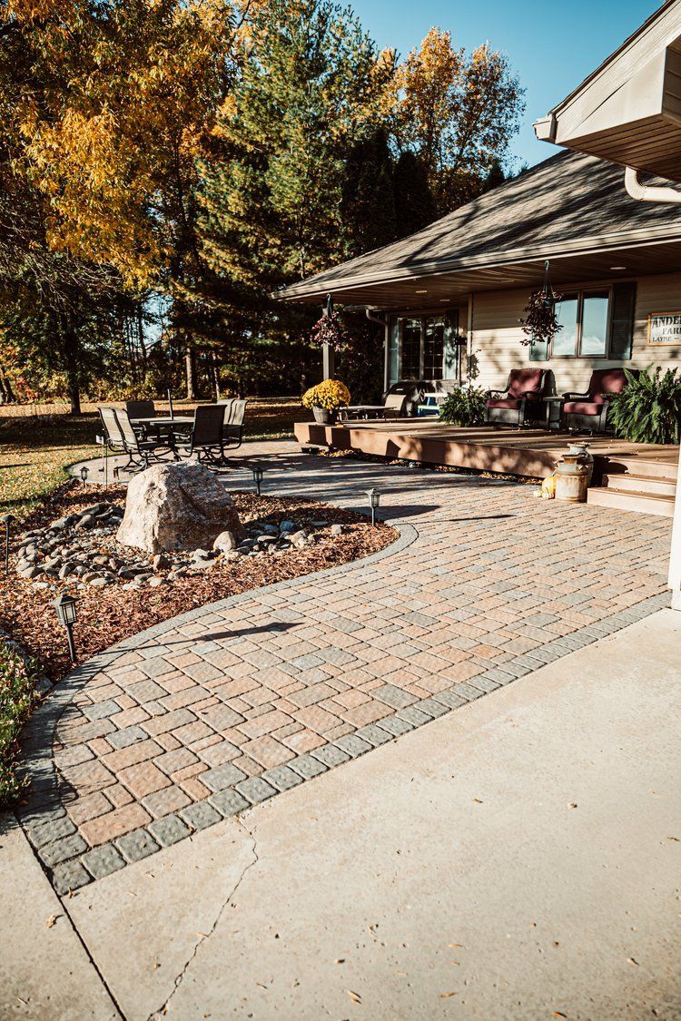 A brick walkway leading to a house with a patio in front of it.