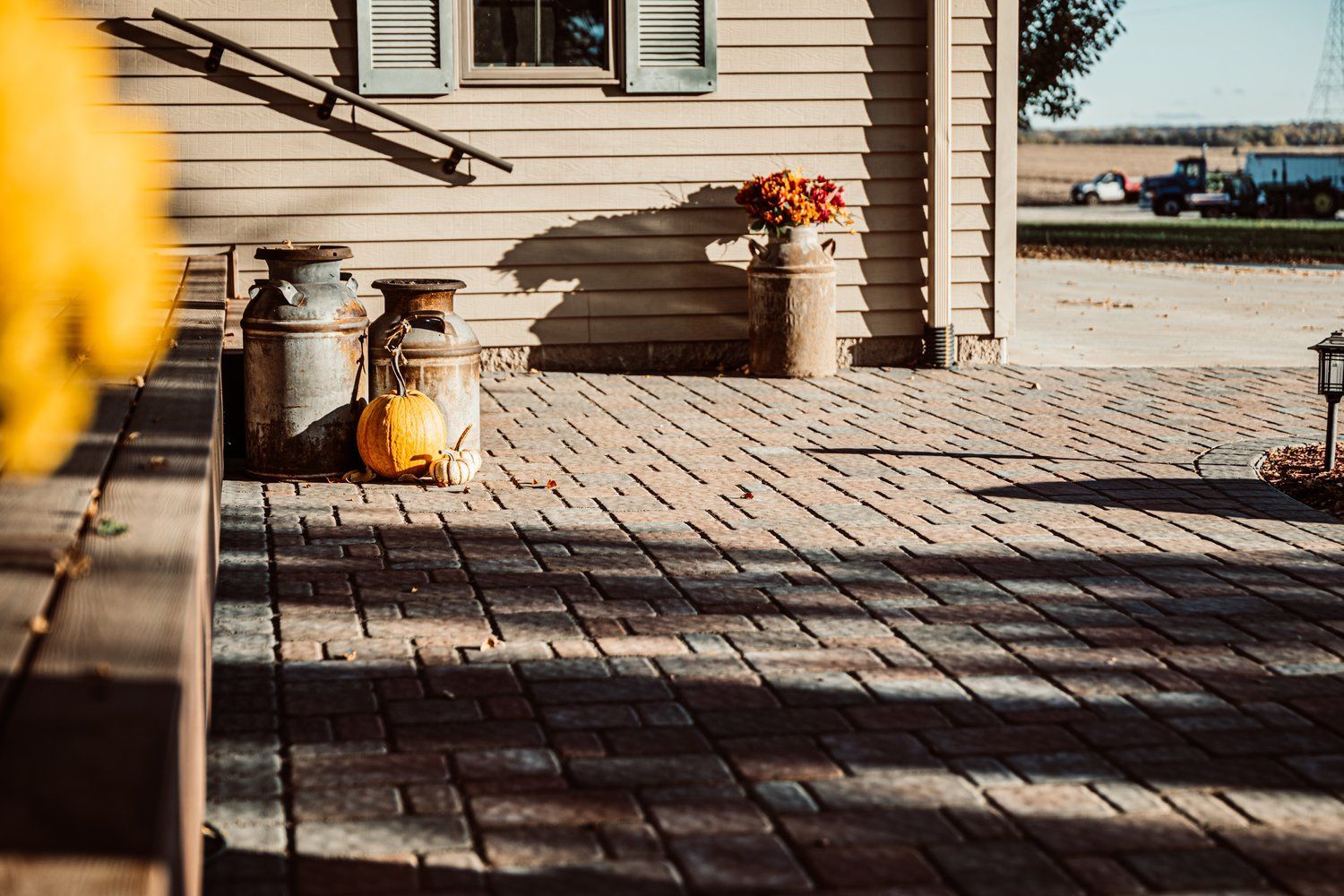 A brick patio with a pumpkin and milk cans in front of a house.
