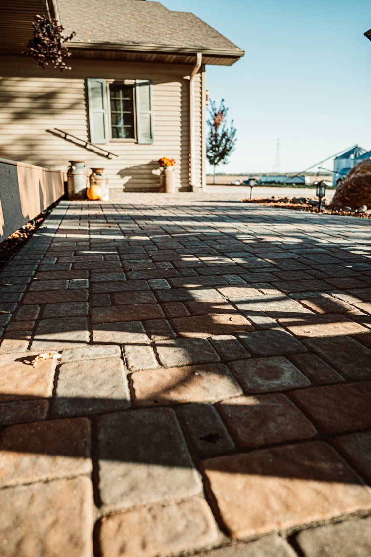 A brick driveway leading to a house on a sunny day.