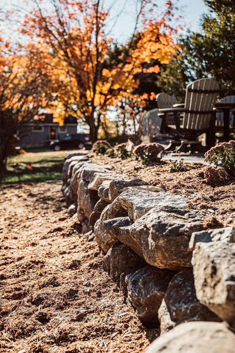 A stone wall in a garden with a table and chairs in the background.