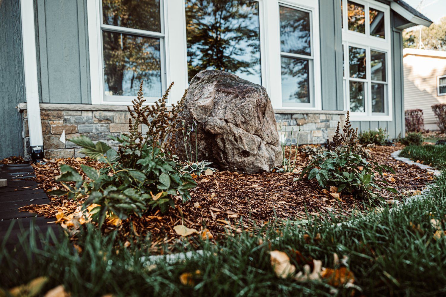 A large rock is sitting in the grass in front of a house.