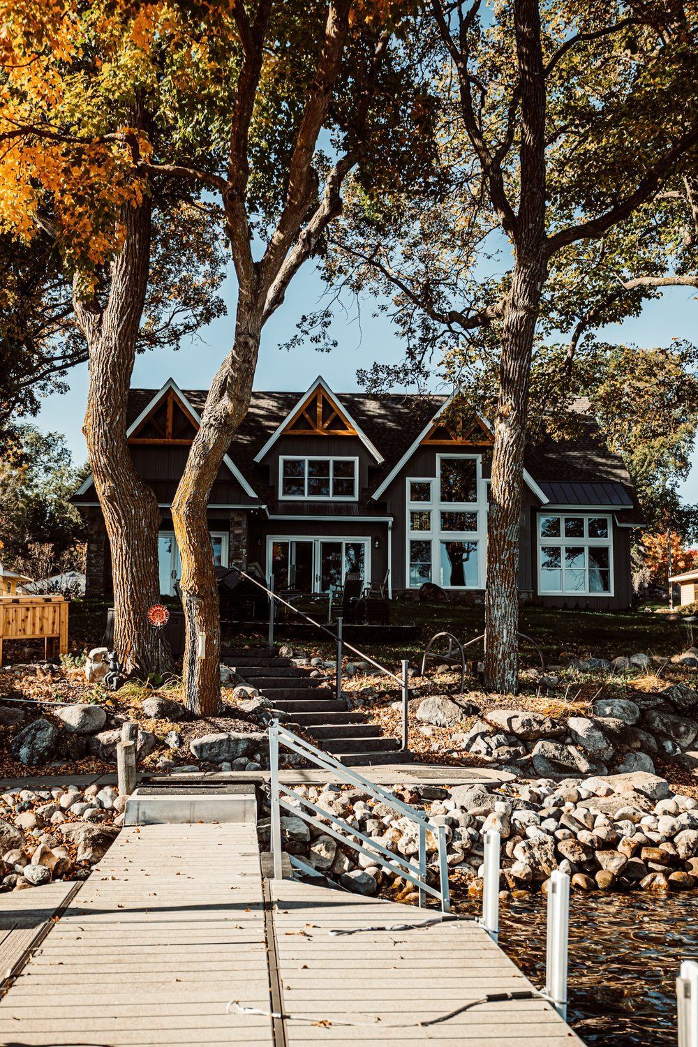 A house with a dock in front of it and trees in the background.