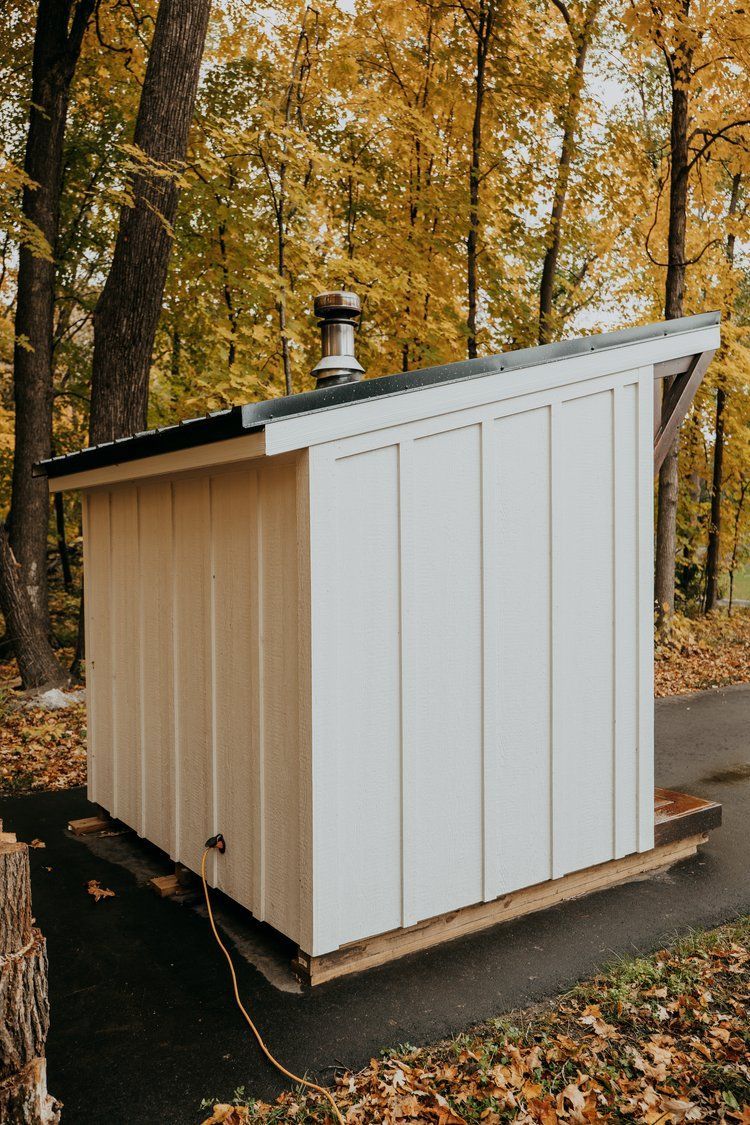 A small white shed is sitting in the middle of a forest.