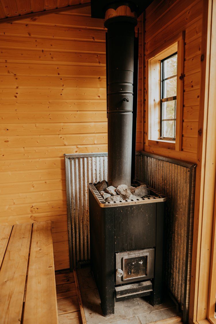 A wood stove is sitting in a wooden room next to a window.