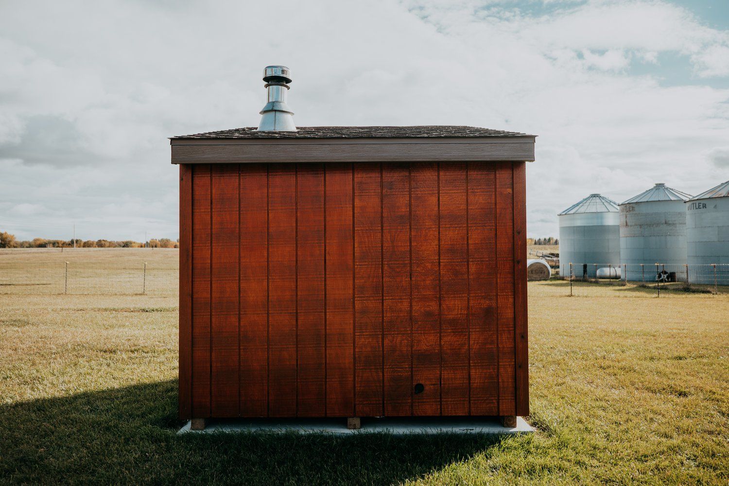 A small wooden shed is sitting in the middle of a grassy field.
