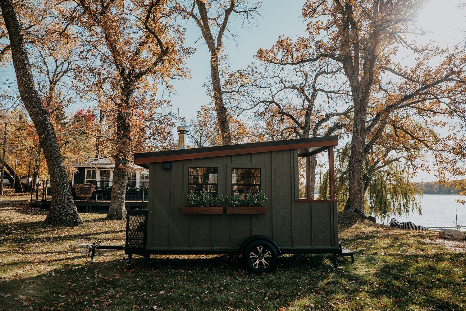 A small house on wheels is parked in a field next to a lake.
