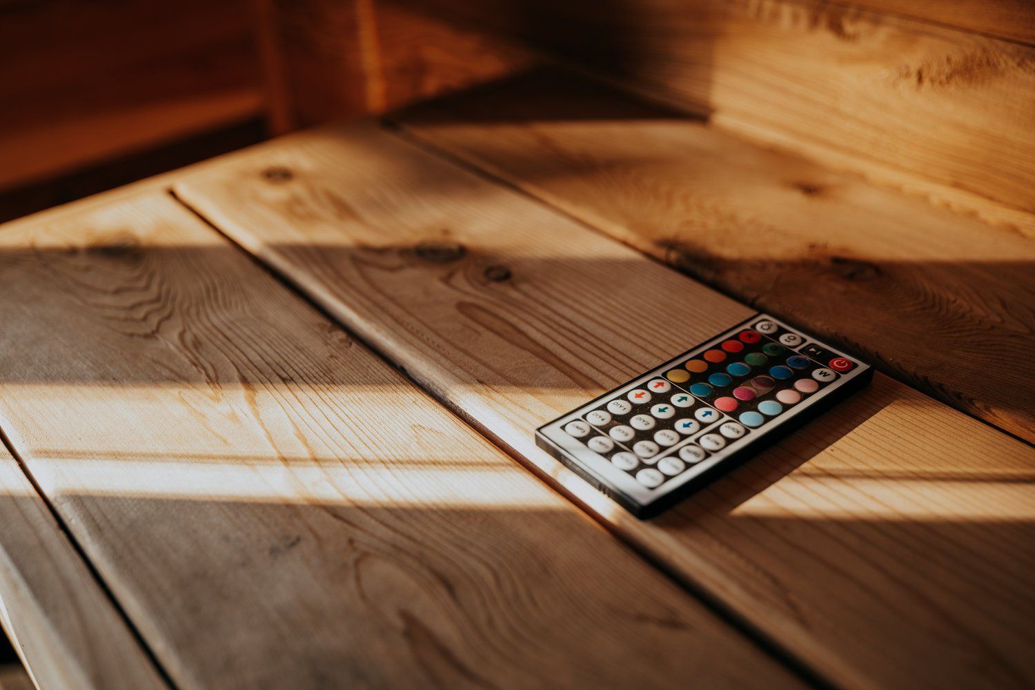 A remote control is sitting on a wooden table.