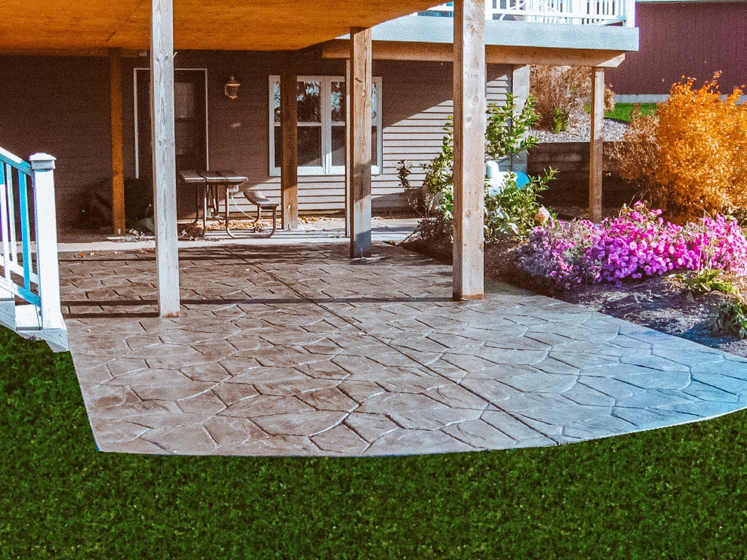 A patio with a pergola and flowers in front of a house.