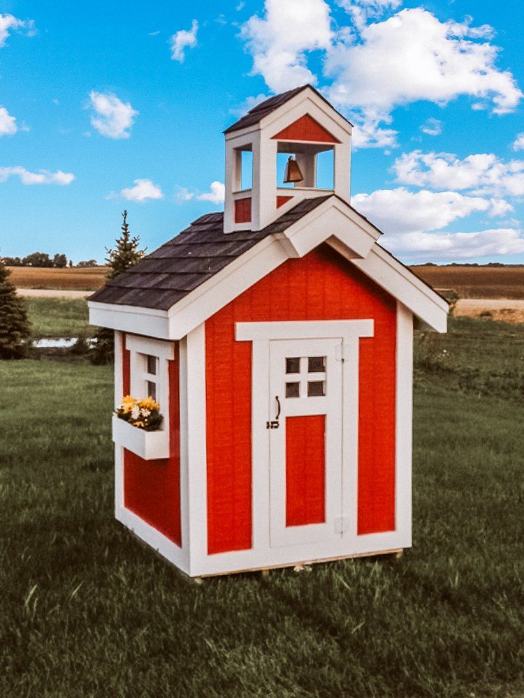 A small red and white playhouse with a bell on top