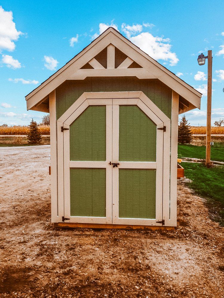 A small green and white shed is sitting in the middle of a dirt field.